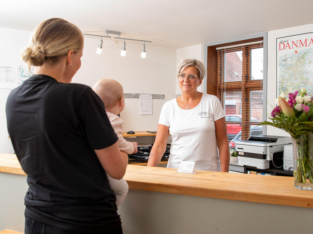 Receptionist Connie byder mor og barn velkommen til Fysioterapeuterne i Nyborg